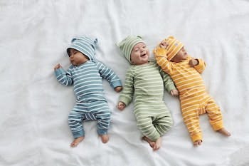 Kolme pientä vauvaa sängyllä joilla raita-asut päällä.